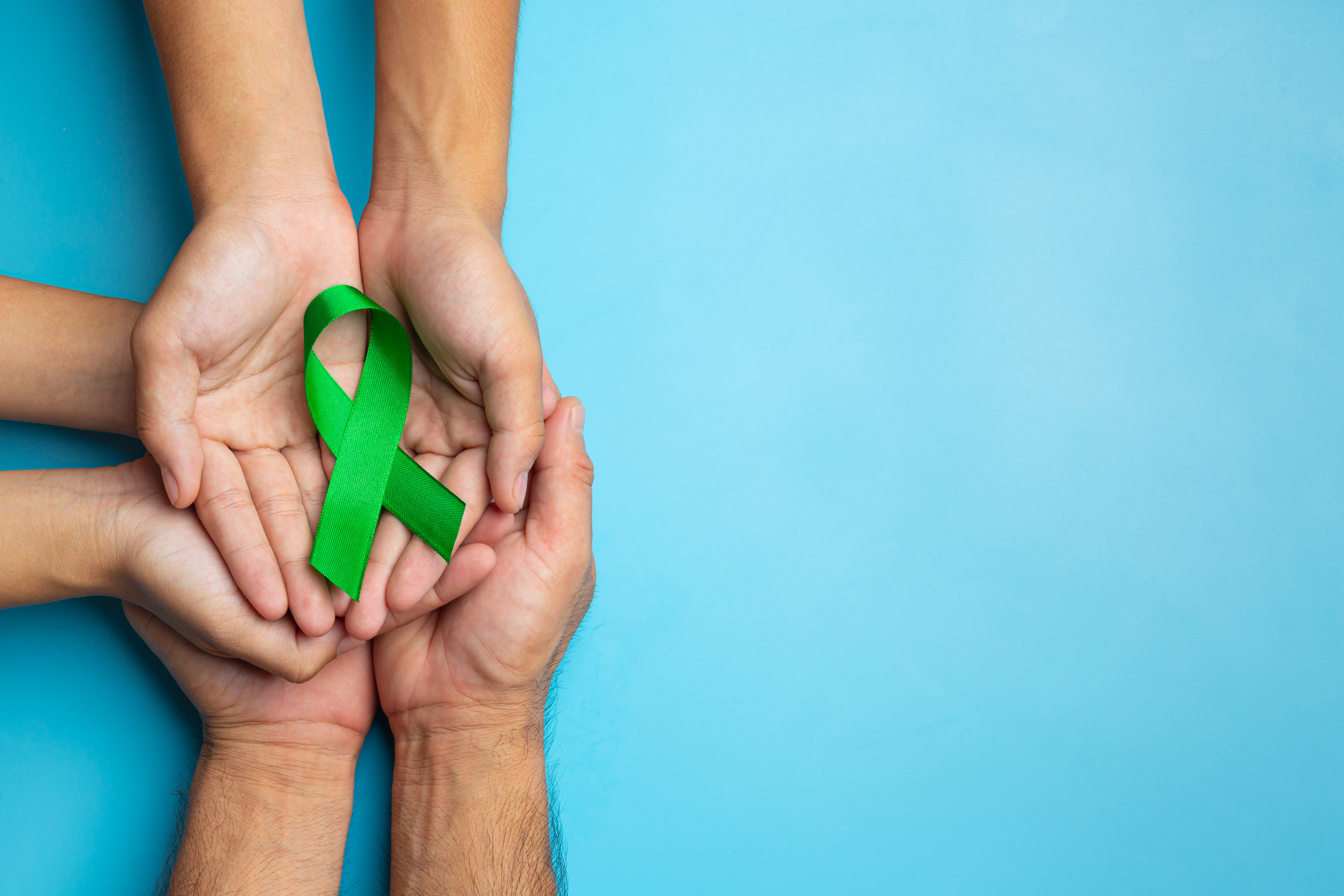 World Mental Health Day; green ribbon put in human's hands on bl