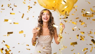 attractive young stylish woman celebrating new year, drinking champagne holding air balloons, golden confetti flying, smiling happy, white background, isolated, wearing party dress