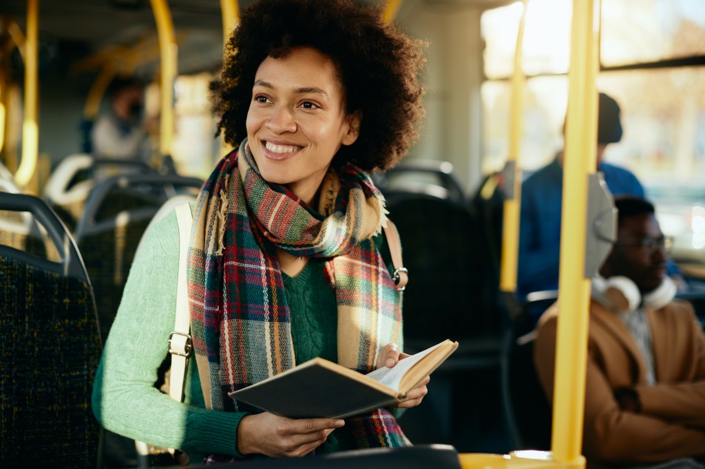 Happy African American woman reading a book while commuting by b