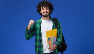 front-view-male-student-wearing-black-backpack-holding-copybooks-files-blue-wall