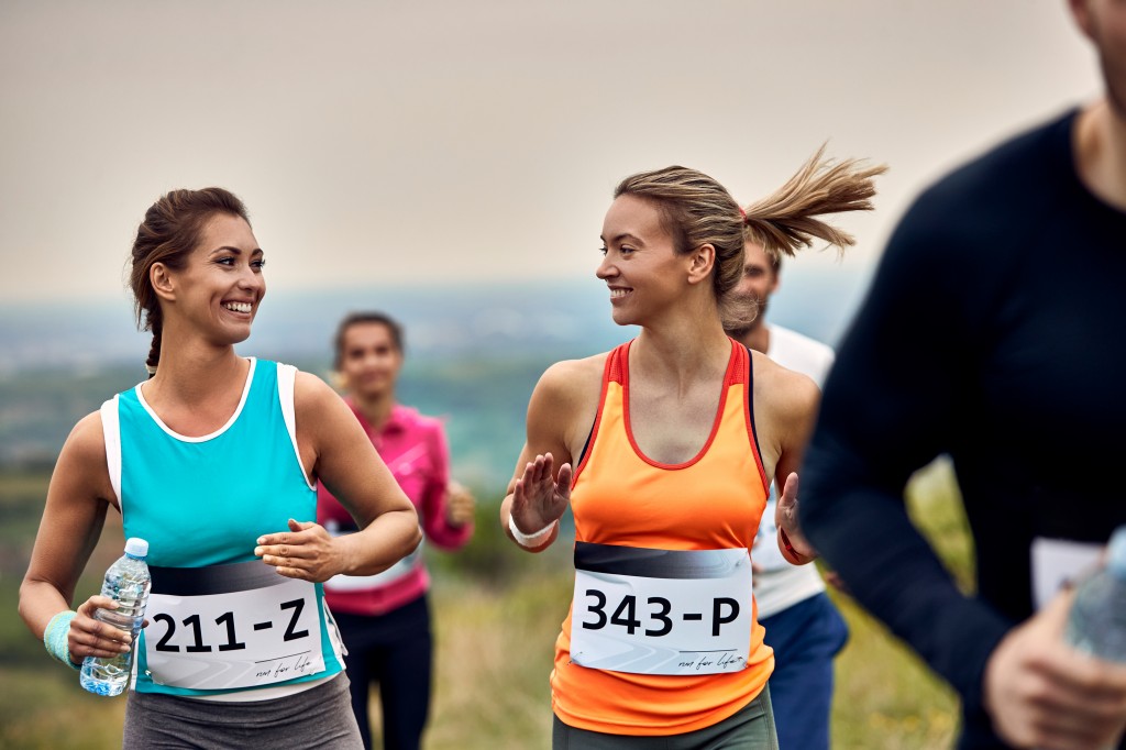 Happy athletic women talking while running a marathon in nature.