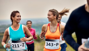 Happy athletic women talking while running a marathon in nature.