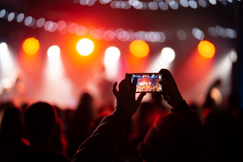 Person close up of recording video with smartphone during a concert.