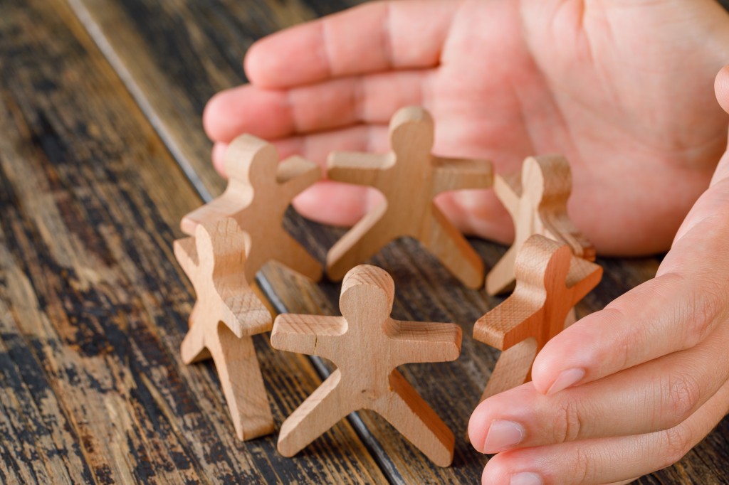 Business success concept on wooden background high angle view. hands protecting wooden figures of people.