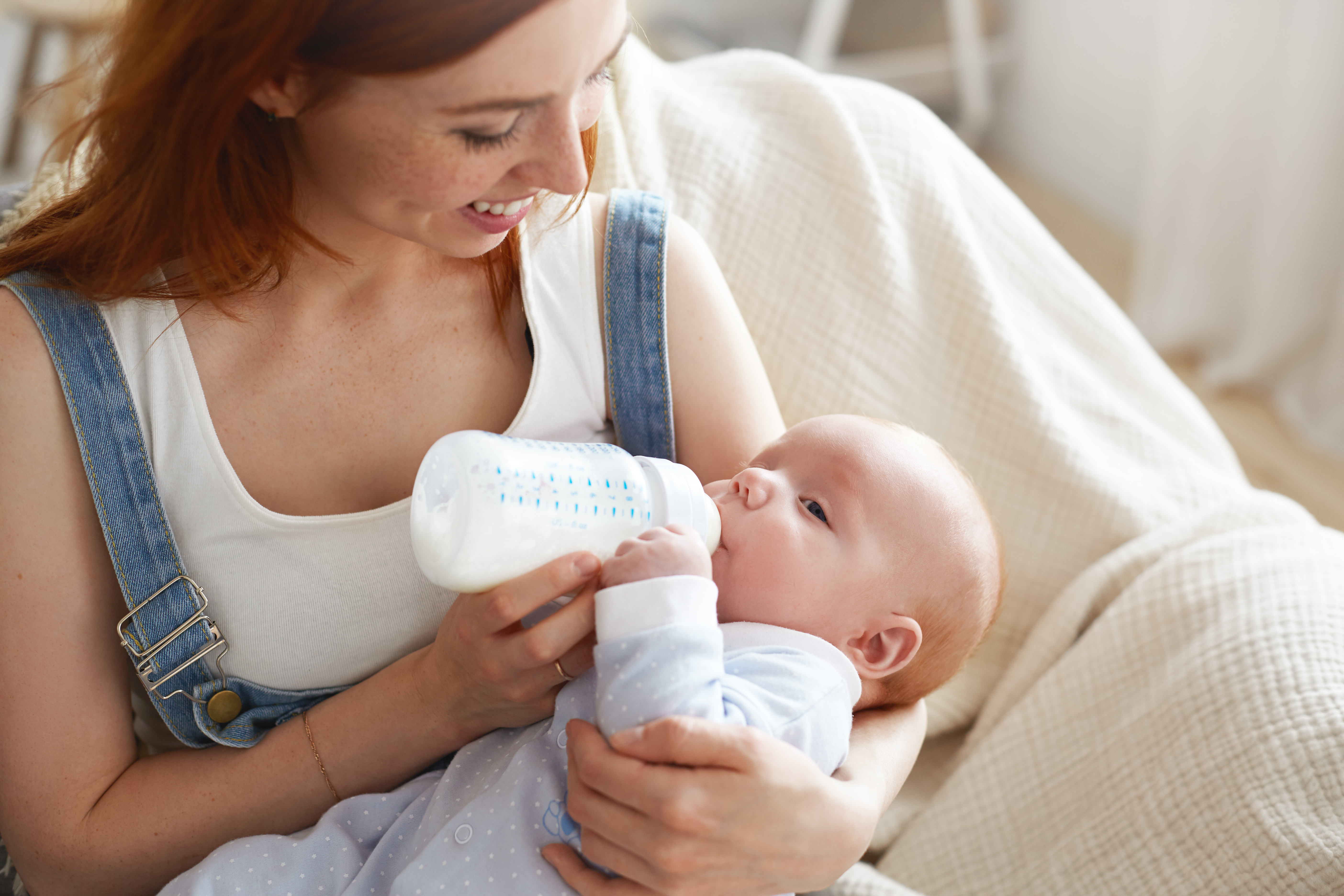 Sweet moment of happy young Caucasian mother smiling joyfully holding bottle of modified milk and feeding her adorable baby. People, lifestyle, childcare, maternity, love, family and happiness concept