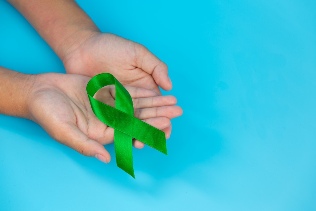 World Mental Health Day; green ribbon put in human's hands on bl