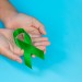 World Mental Health Day; green ribbon put in human's hands on bl