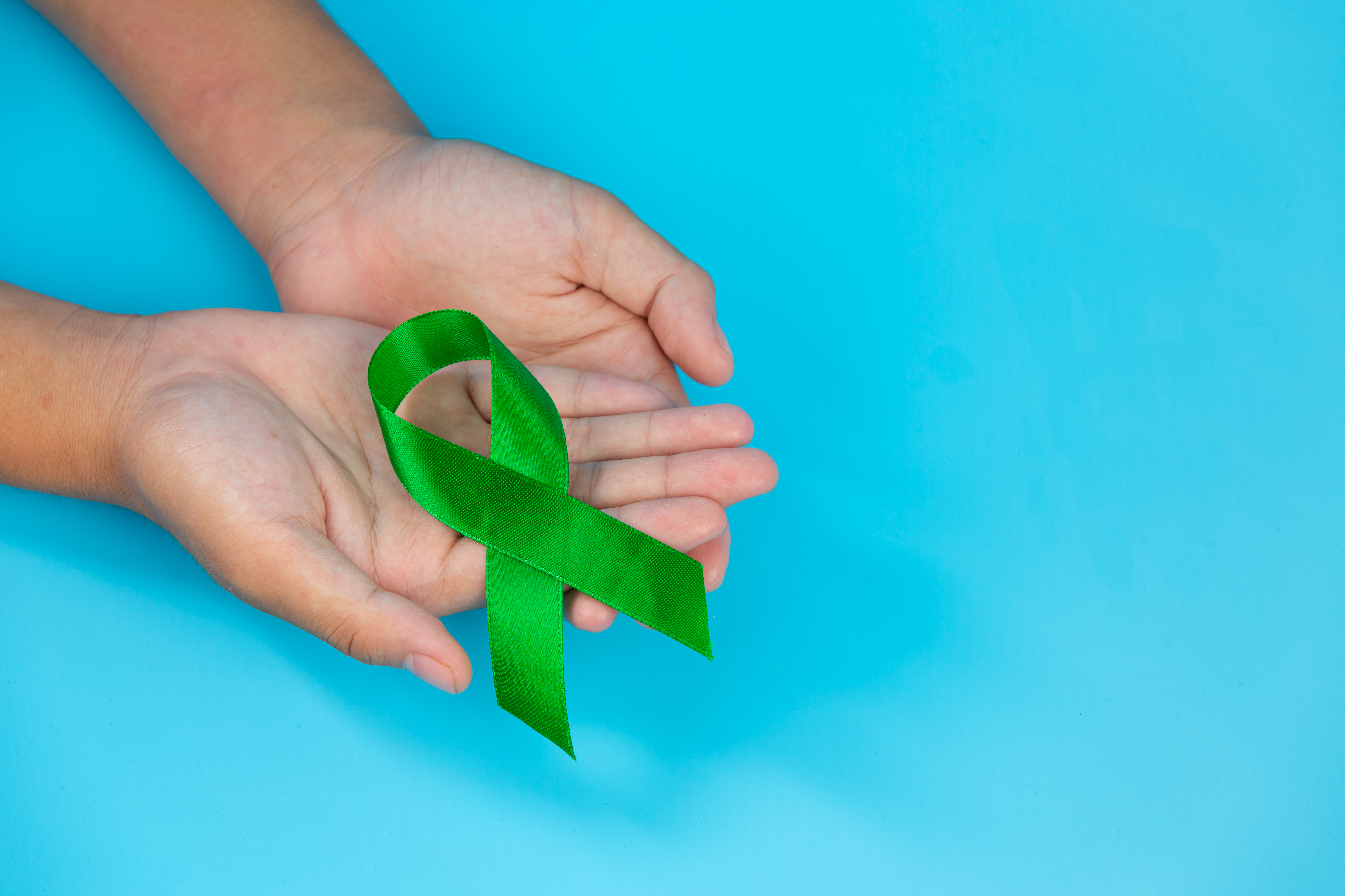 World Mental Health Day; green ribbon put in human's hands on bl