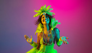 Beautiful young woman in carnival and masquerade costume on gradient studio background in neon light