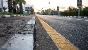 City asphalt road with palm trees along the road at sunset.