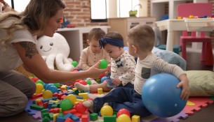 Teacher and preschool students playing with balls sitting on floor at kindergarten