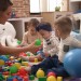 Teacher and preschool students playing with balls sitting on floor at kindergarten