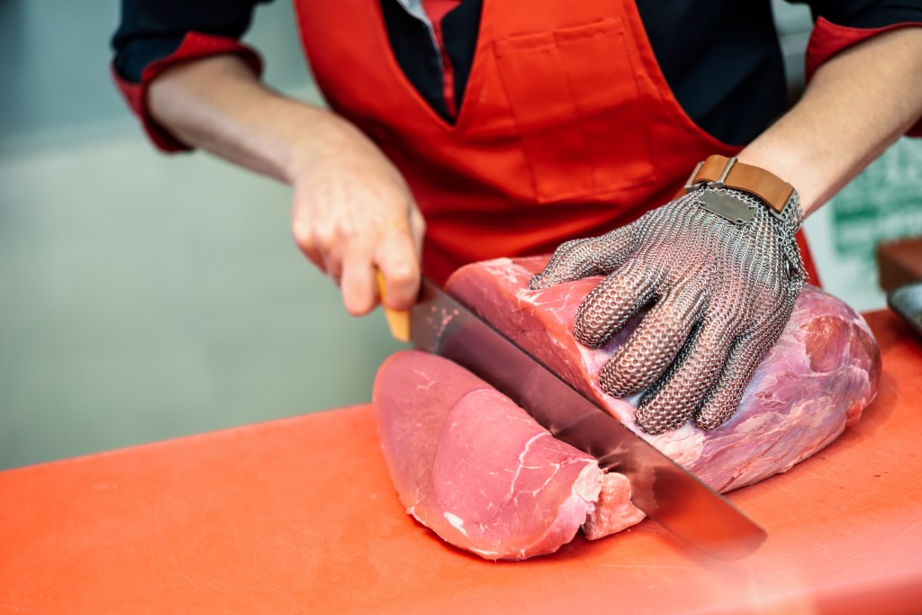 Woman cutting fresh meat in a butcher shop with metal safety mes