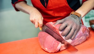 Woman cutting fresh meat in a butcher shop with metal safety mes