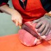 Woman cutting fresh meat in a butcher shop with metal safety mes