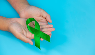 World Mental Health Day; green ribbon put in human's hands on bl