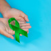 World Mental Health Day; green ribbon put in human's hands on bl